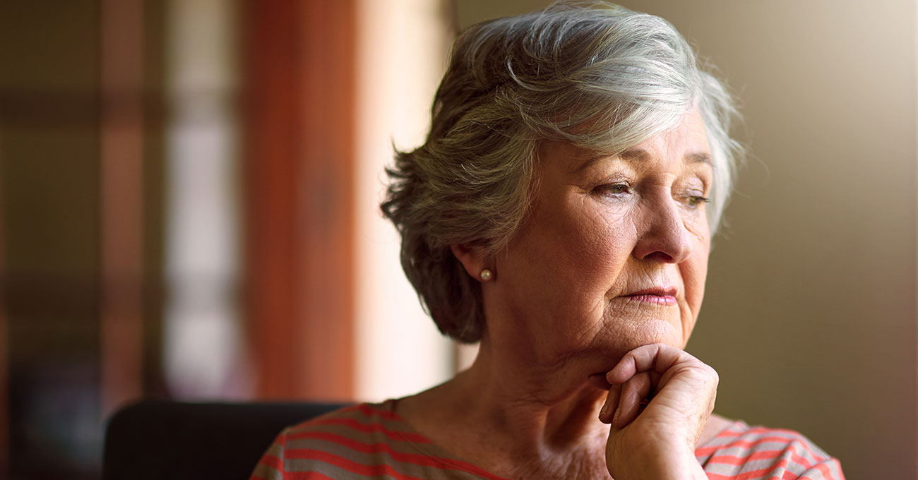 Eine ältere Dame mit grauen kurzen Haaren schaut nachdenklick aus dem Fenster.